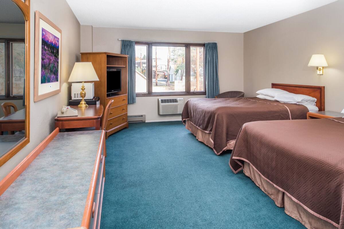 Ein Hotelzimmer mit zwei Betten, einem Schreibtisch mit Lampe, einem Fernseher und einem großen Spiegel.