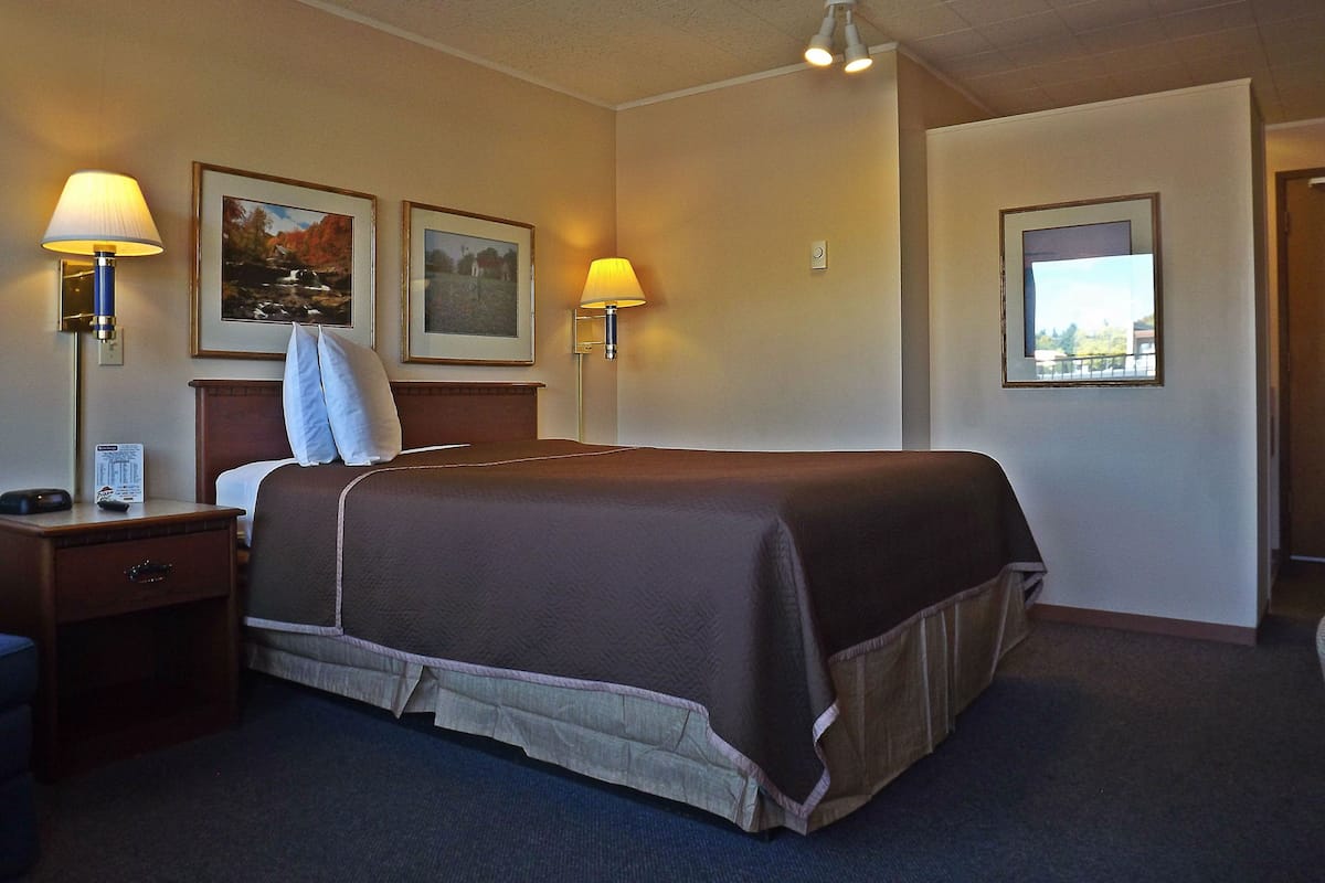 Ein Hotelzimmer mit einem Bett, zwei Wandleuchten, einem Nachttisch, einem gerahmten Bild und einem Fenster.