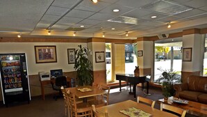 A dining area with a vending machine, wooden tables, chairs, a piano, and framed pictures on the walls. - Travelodge by Wyndham Kalispell (Kalispell)