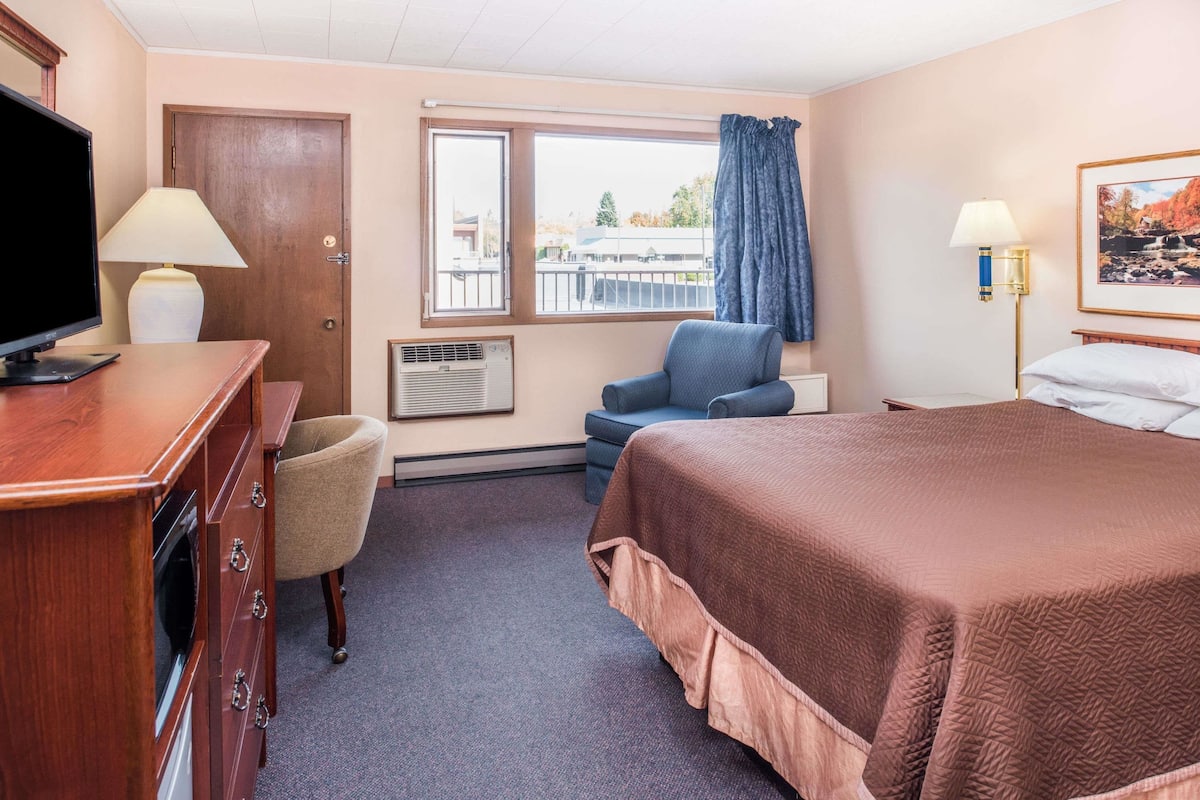 Ein Hotelzimmer mit Bett, Schreibtisch mit Fernseher, Sessel, Fenster mit Blick und einem Bild an der Wand.