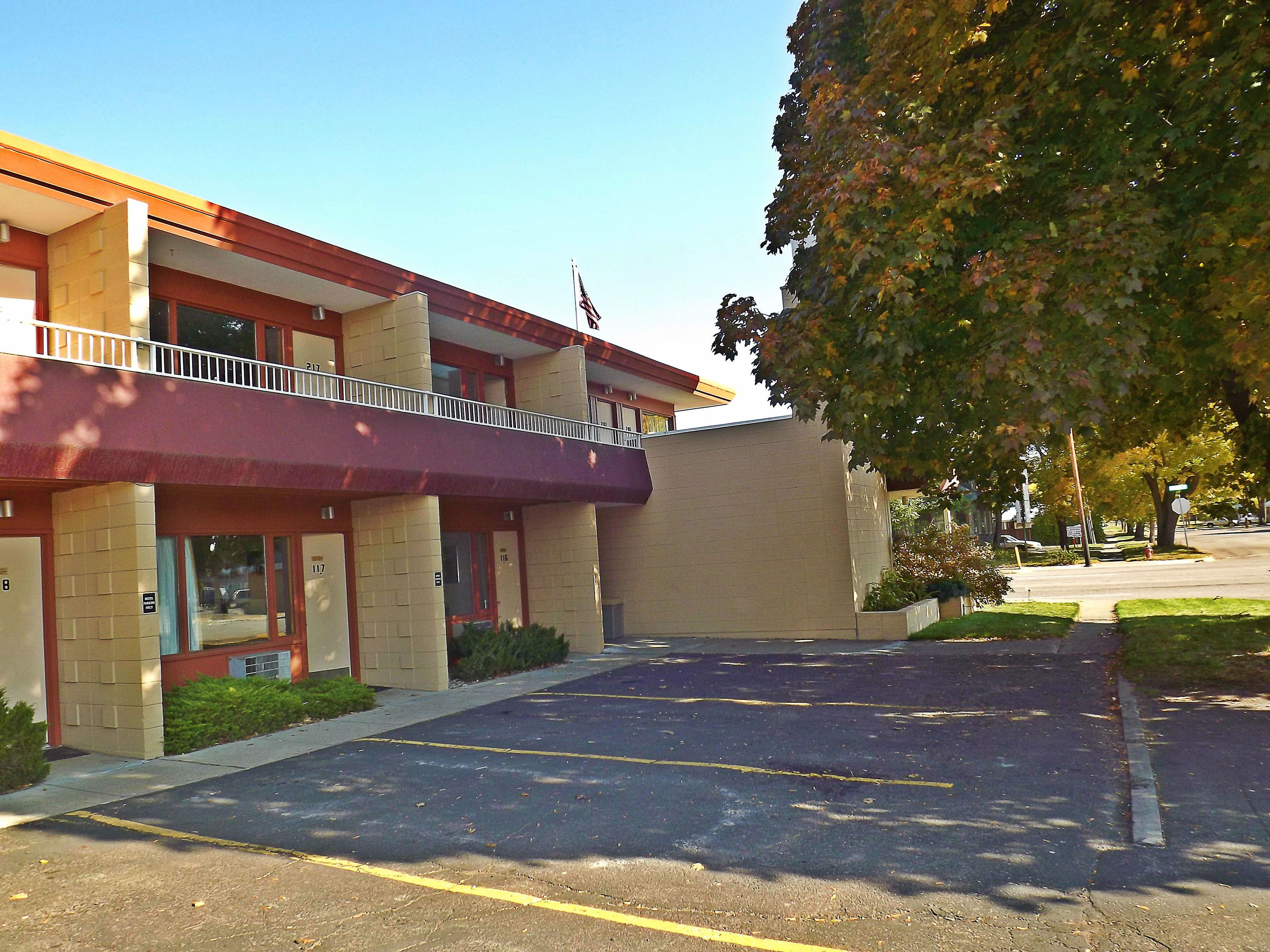 Un edificio con toldo rojo, estacionamiento y un árbol con hojas otoñales.