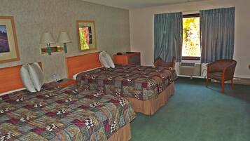A hotel room with two beds, a desk, a chair, a lamp, and a window with curtains.