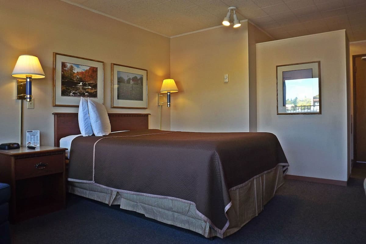 Ein Hotelzimmer mit einem Bett, zwei Nachttischlampen, einem Nachttisch, einem gerahmten Bild und einem Fenster.