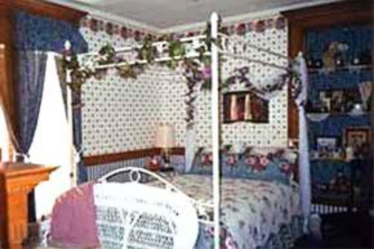 A bedroom with a four-poster bed, floral wallpaper, and a dresser.