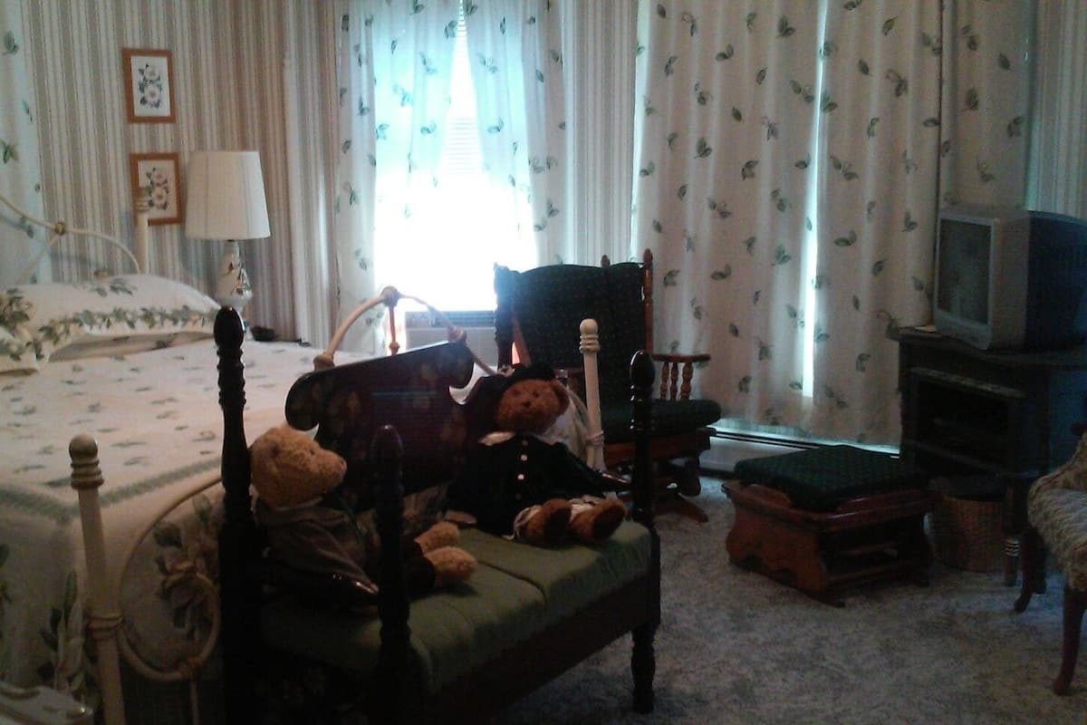 A bedroom with a bed, a chair, a television, and stuffed animals.