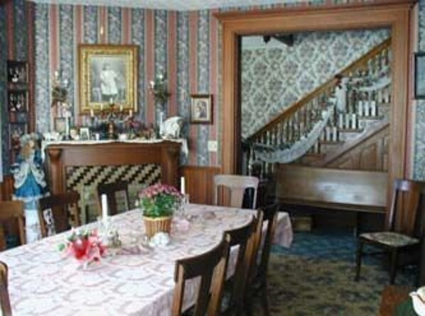 A dining room with a wooden staircase, a table set with flowers, and a portrait on the wall.