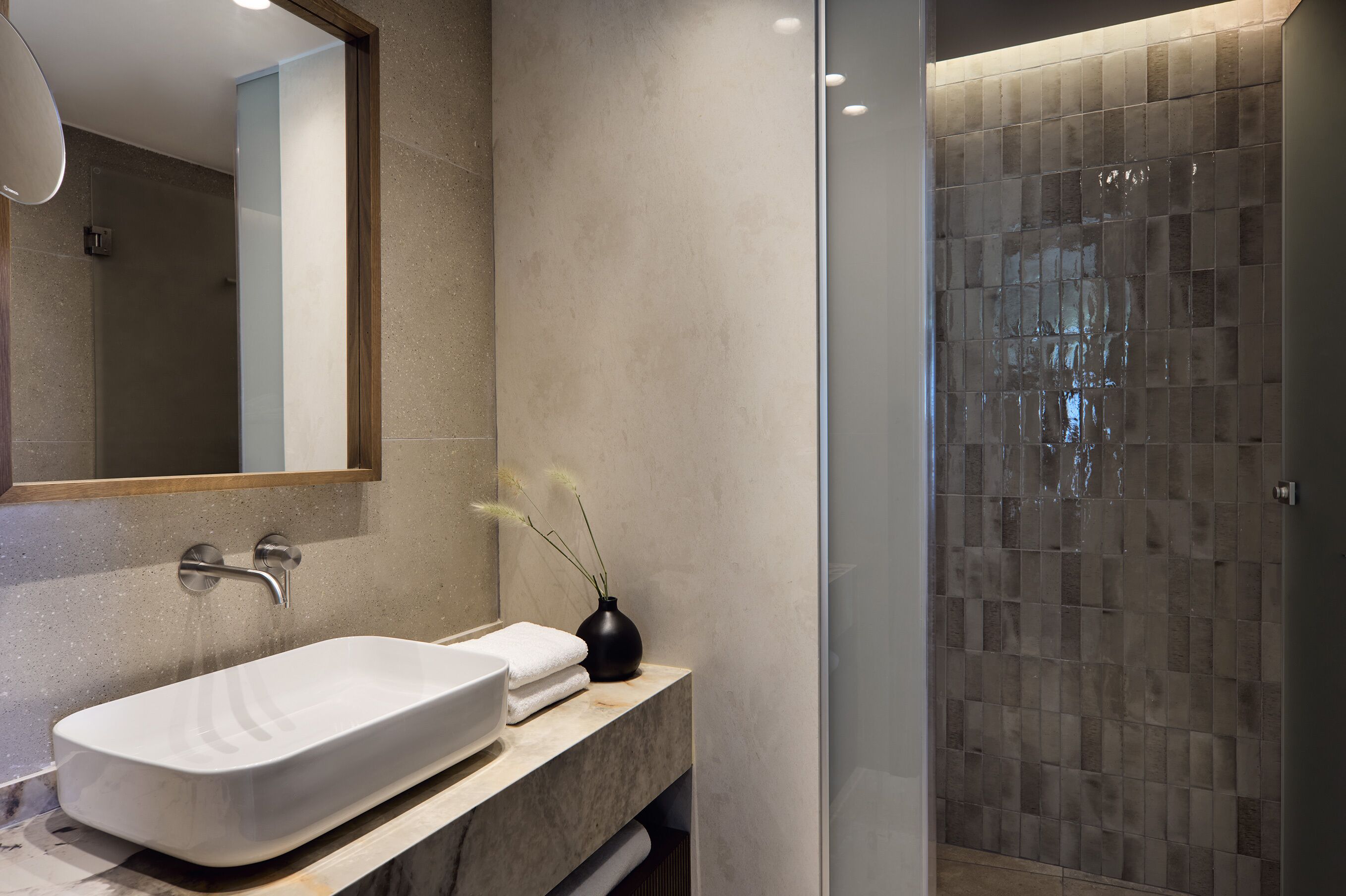 A modern bathroom with a large white sink, a mirror, and a shower area with tiled walls.