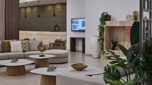 A modern interior with a sofa, round tables, a fireplace, and a television. - Atlantica Callisto (Ayia Napa)