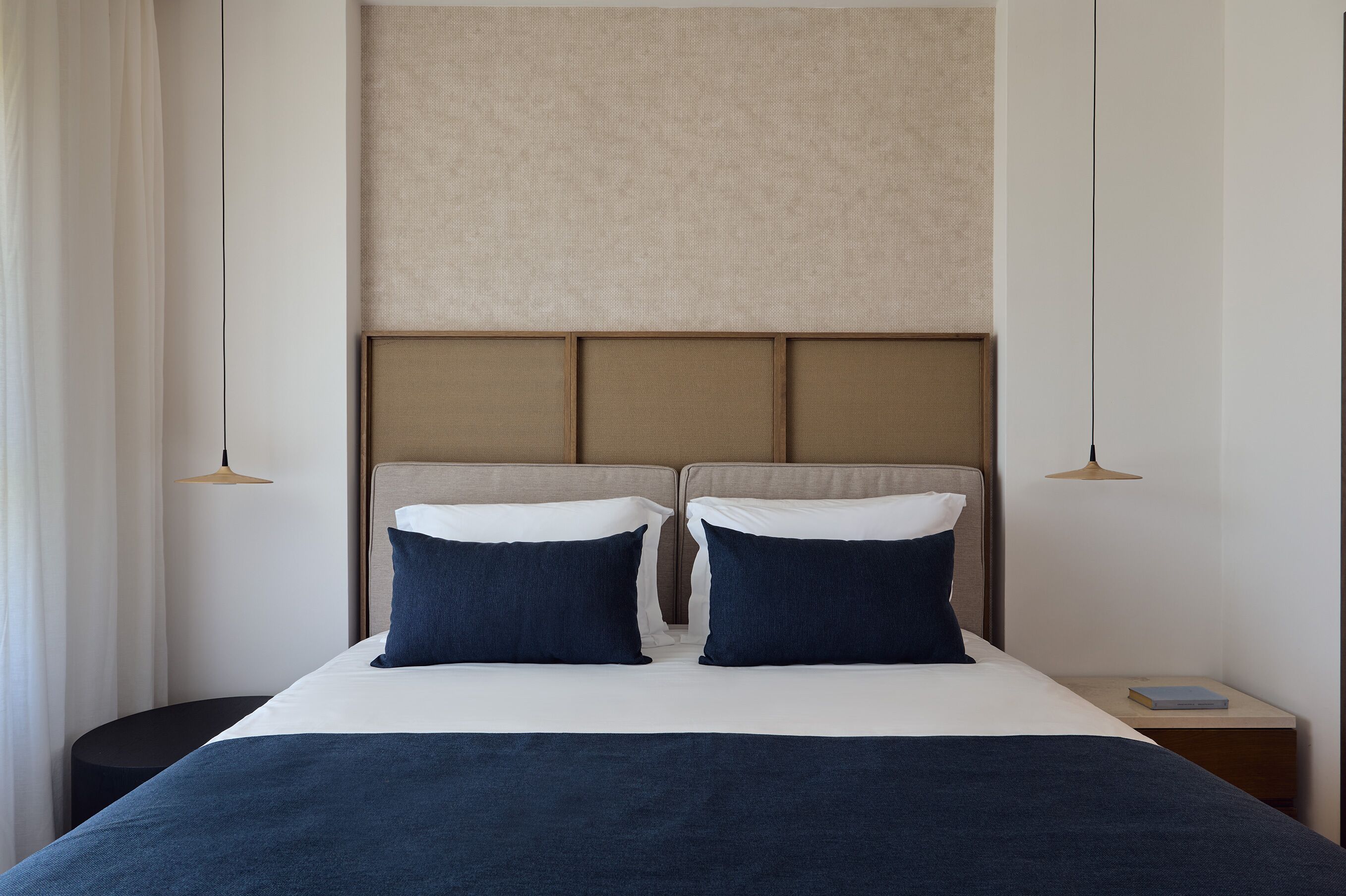 Hotellihuone, jossa on sänky, kaksi tyynyä, yöpöytä ja lamppu.
