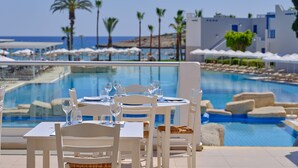 A poolside dining area with tables and chairs, overlooking a pool and the sea. - Atlantica Callisto (Ayia Napa)