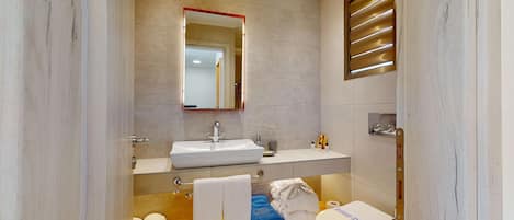 A modern bathroom with a large mirror, a sink, a toilet, and a bathtub.