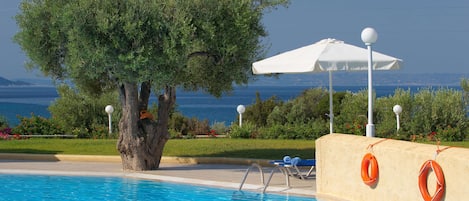 A swimming pool with a lifebuoy, a white umbrella, and a tree.