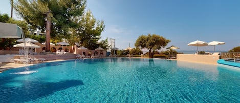 A clear blue pool with lounge chairs and umbrellas, surrounded by trees and a clear sky.