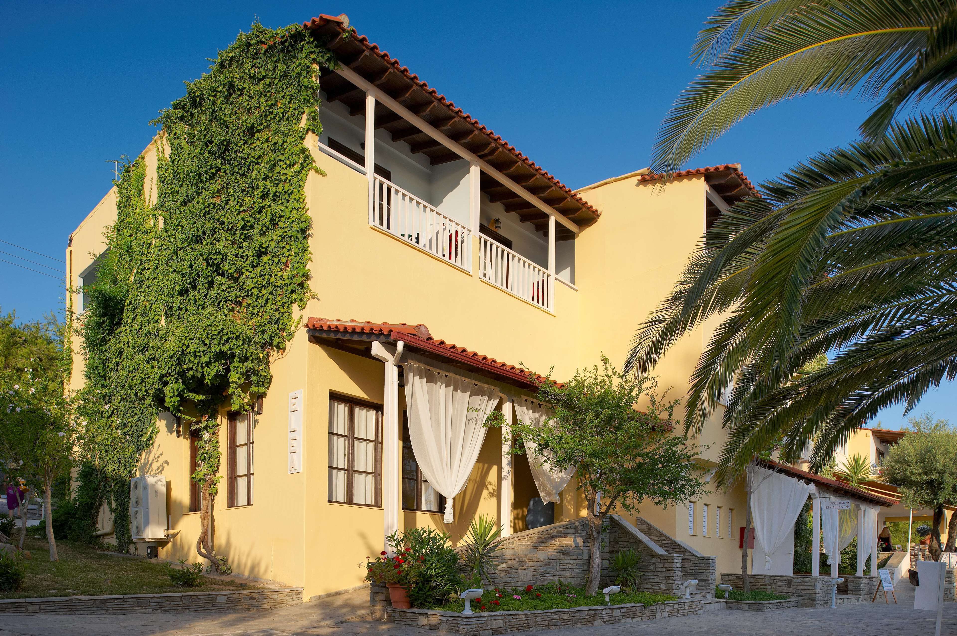 A two-story building with a balcony, a stone wall, and a small garden with potted plants.