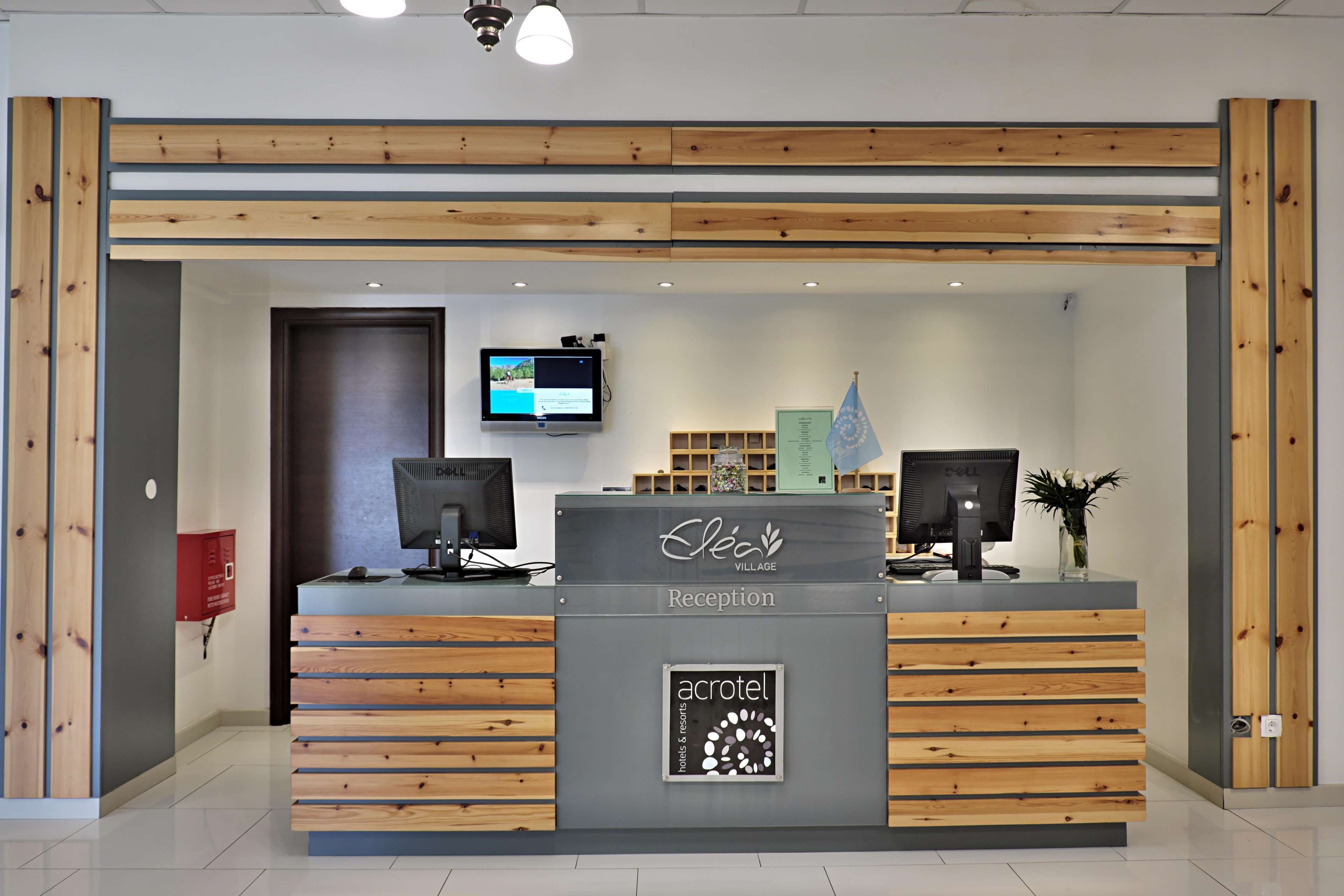Un comptoir d’accueil au design en bois, un écran et une enseigne indiquant « Acrotel Hotels & Resorts ».