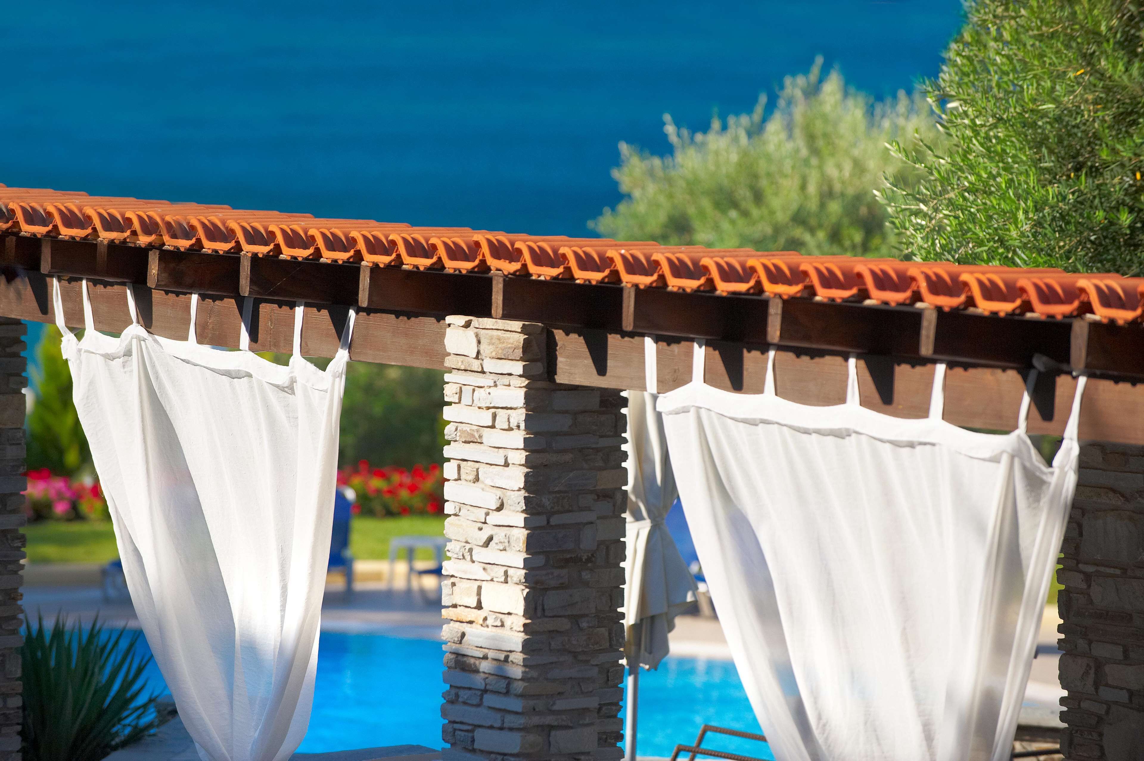 A poolside area with a pergola structure, stone pillars, and a tiled roof.
