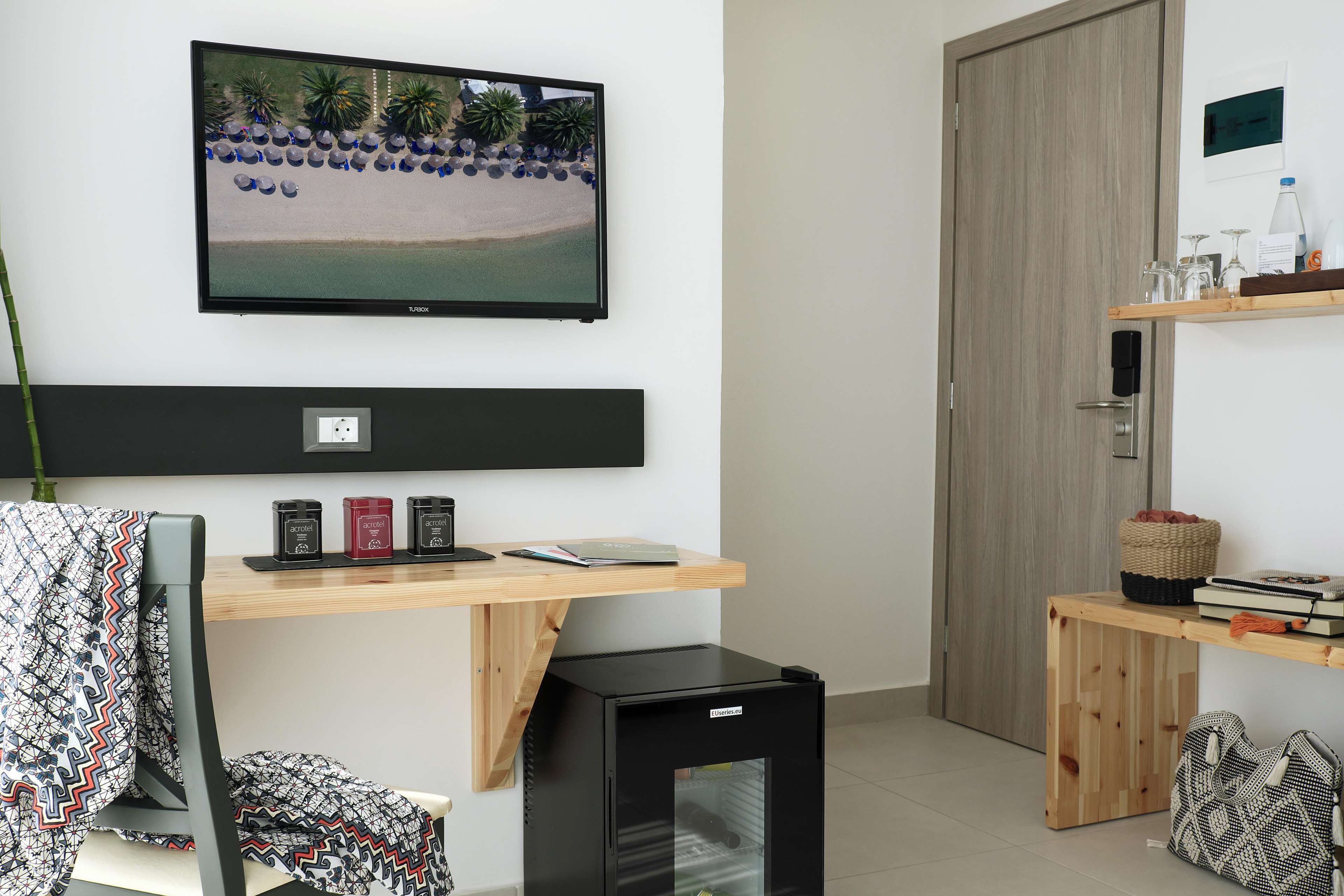 Een moderne kamer met een flatscreen-televisie, een bureau met een laptop, een kleine zwarte koelkast en een houten deur.