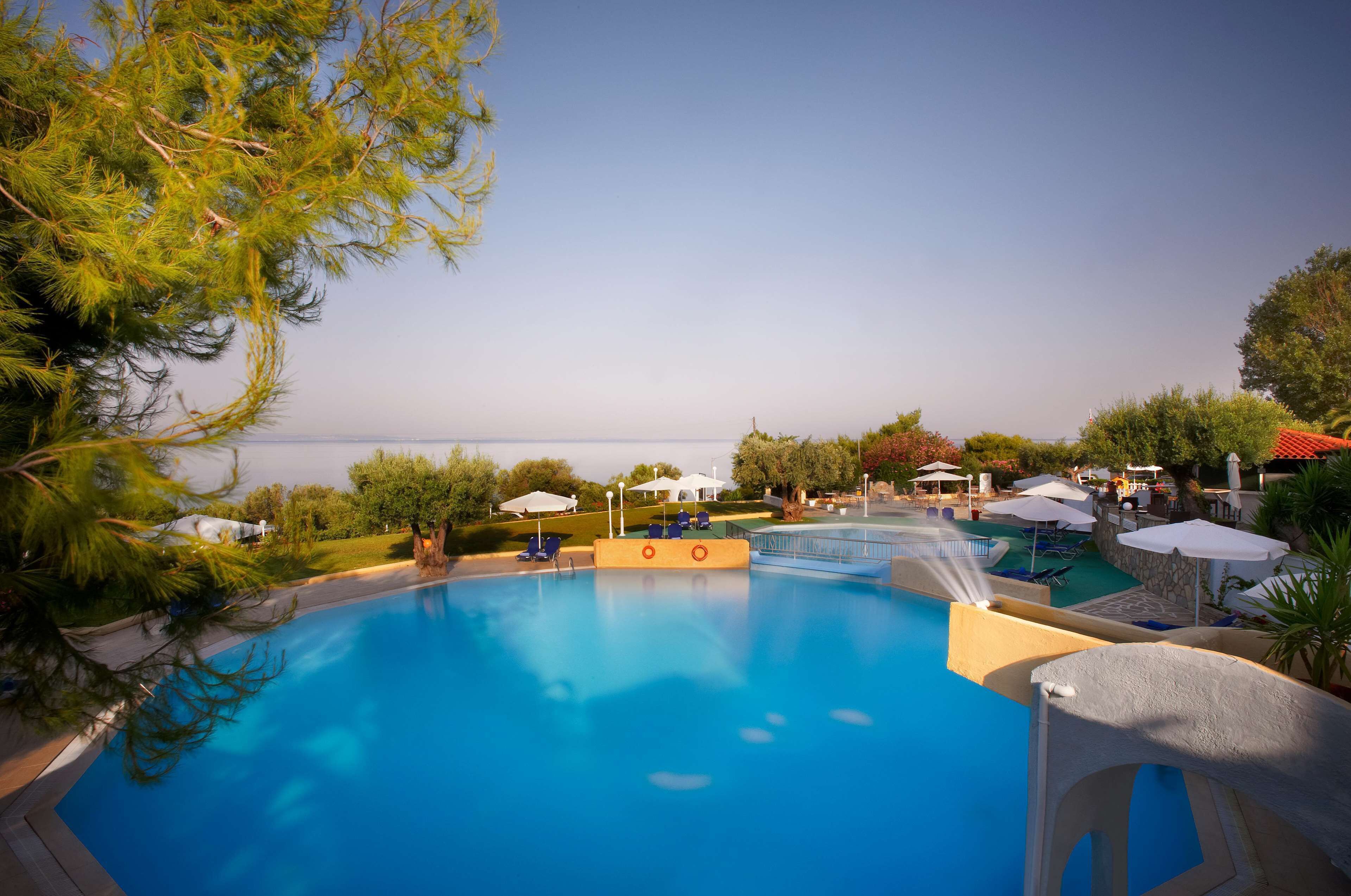A swimming pool with a view of the sea, surrounded by umbrellas and lounge chairs.