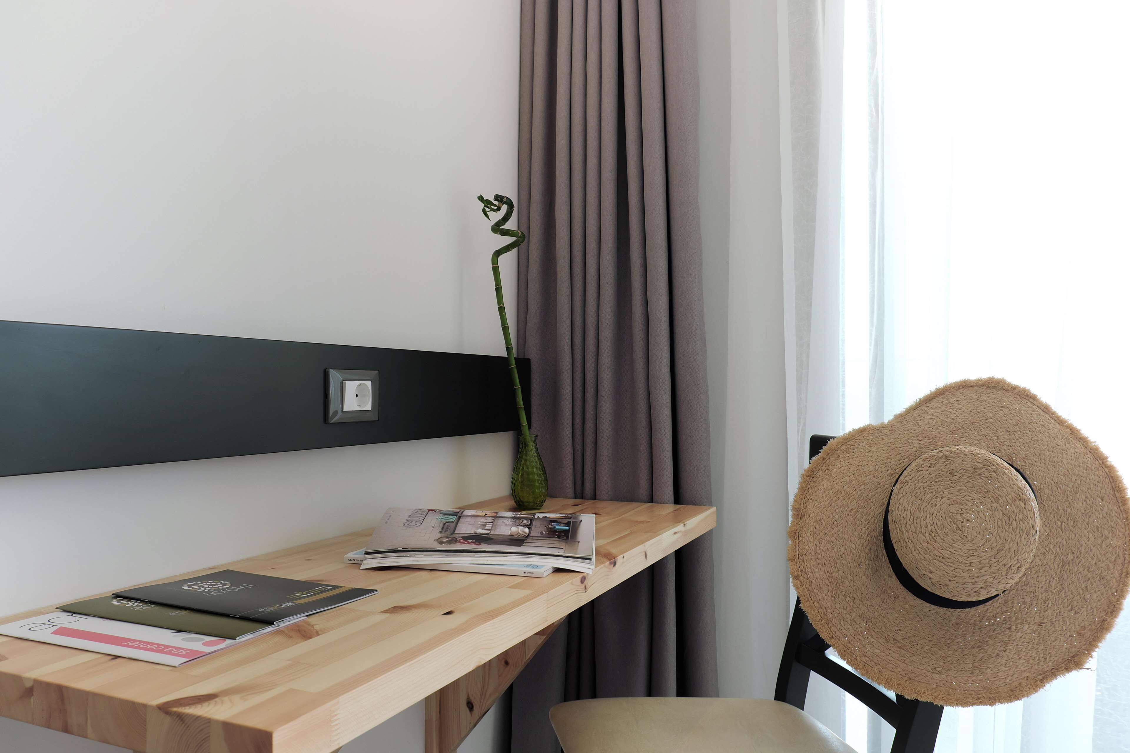 Escritorio de madera con un jarrón de orquídeas verdes, un sombrero de paja y algunas revistas.