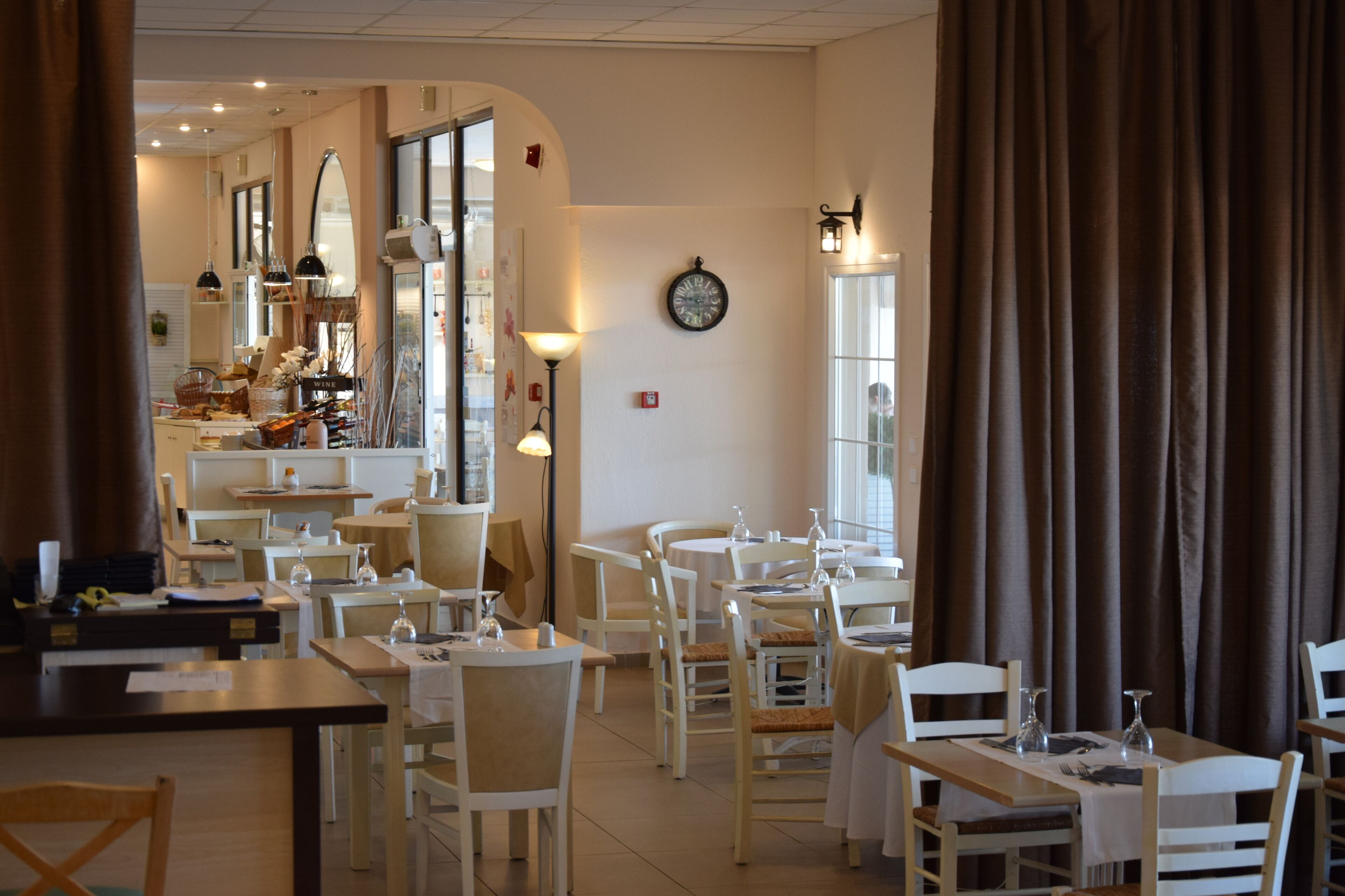 L’intérieur d’un restaurant, avec des tables et des chaises, une horloge au mur et une fenêtre avec des rideaux.