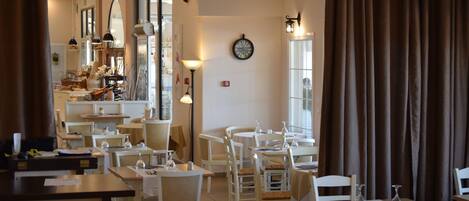 A restaurant interior with tables and chairs, a clock on the wall, and a window with curtains.