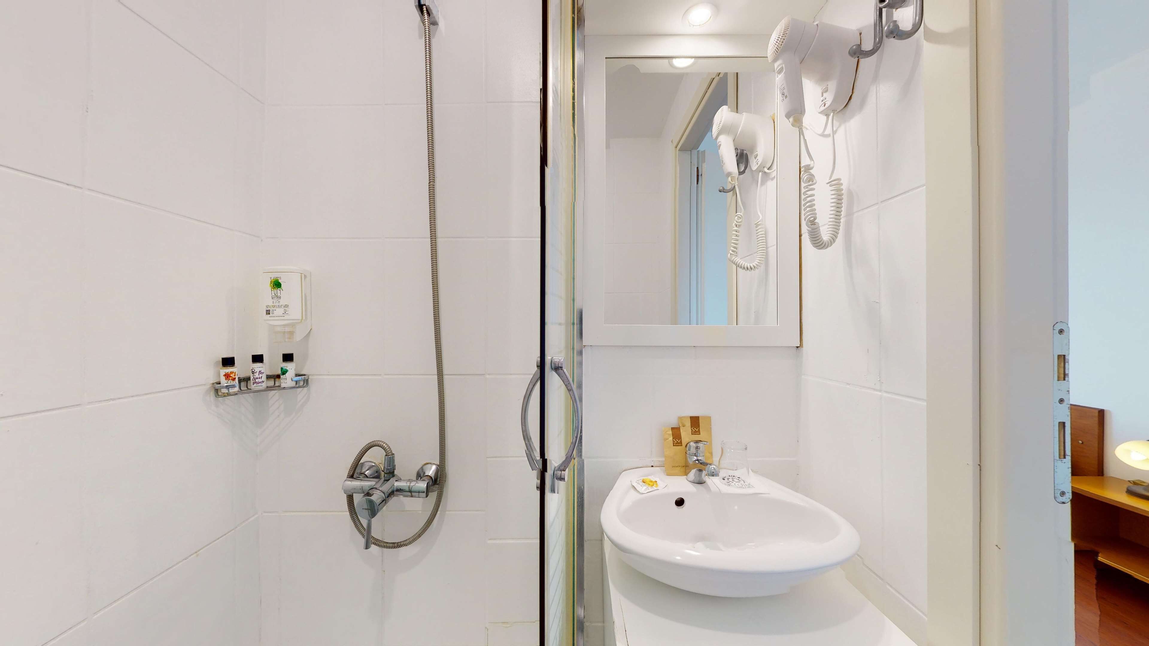 A modern bathroom with a glass-enclosed shower, a white sink with a soap dispenser, and a hairdryer mounted on the wall.