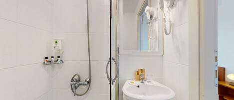 A modern bathroom with a glass-enclosed shower, a white sink with a soap dispenser, and a hairdryer mounted on the wall.