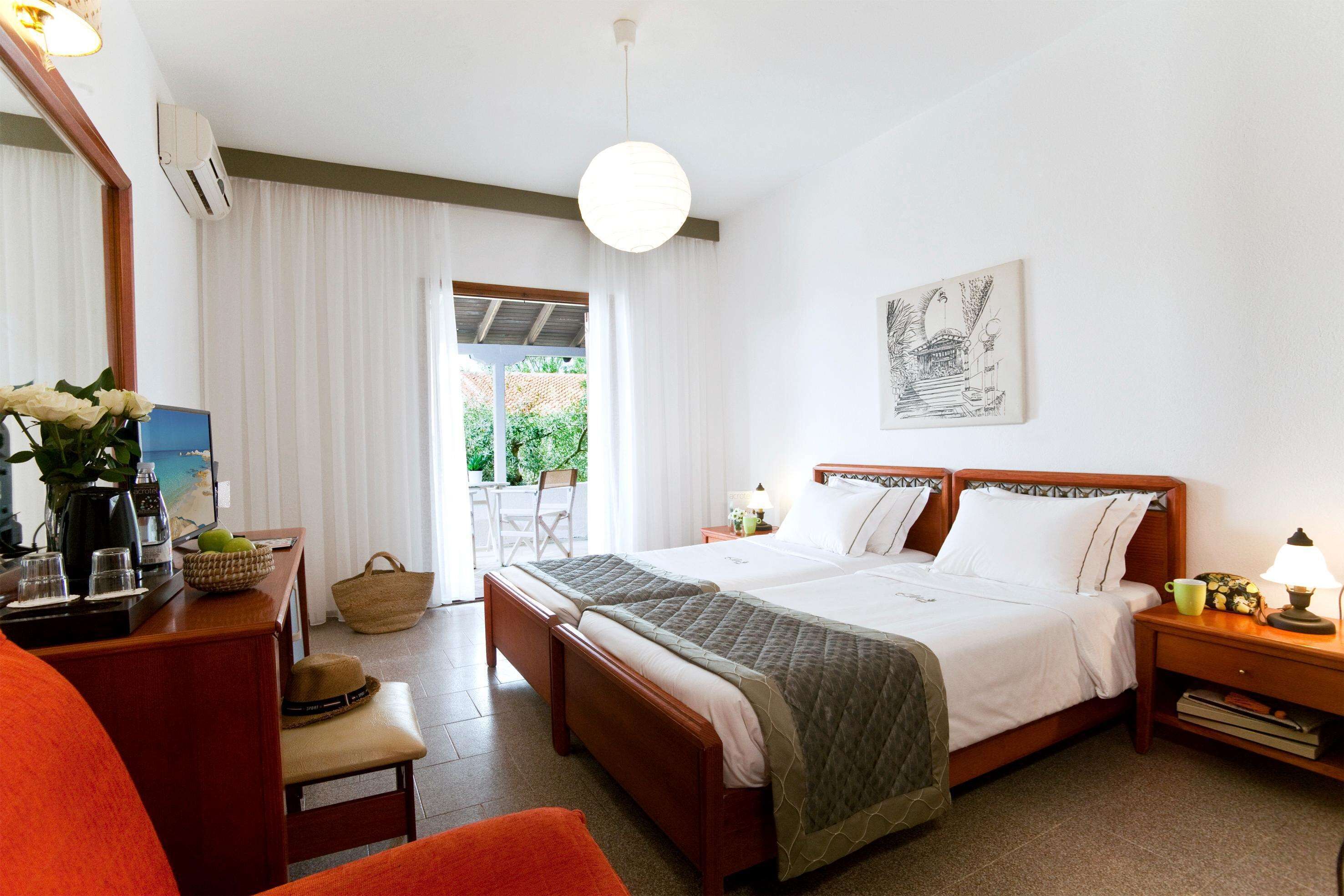A hotel room with a large bed, a desk with a chair, a small table with a lamp, and a window with curtains.