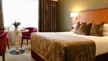 A hotel room with a large bed, a round table with a vase of flowers, a red chair, and a window with curtains.