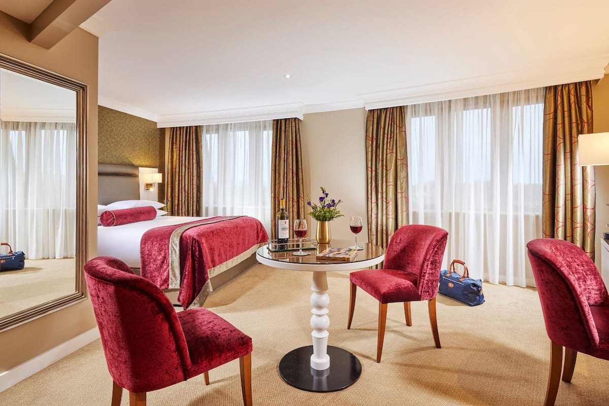 Habitación de hotel con cama, una mesa redonda con sillas, un espejo y una ventana con cortinas.
