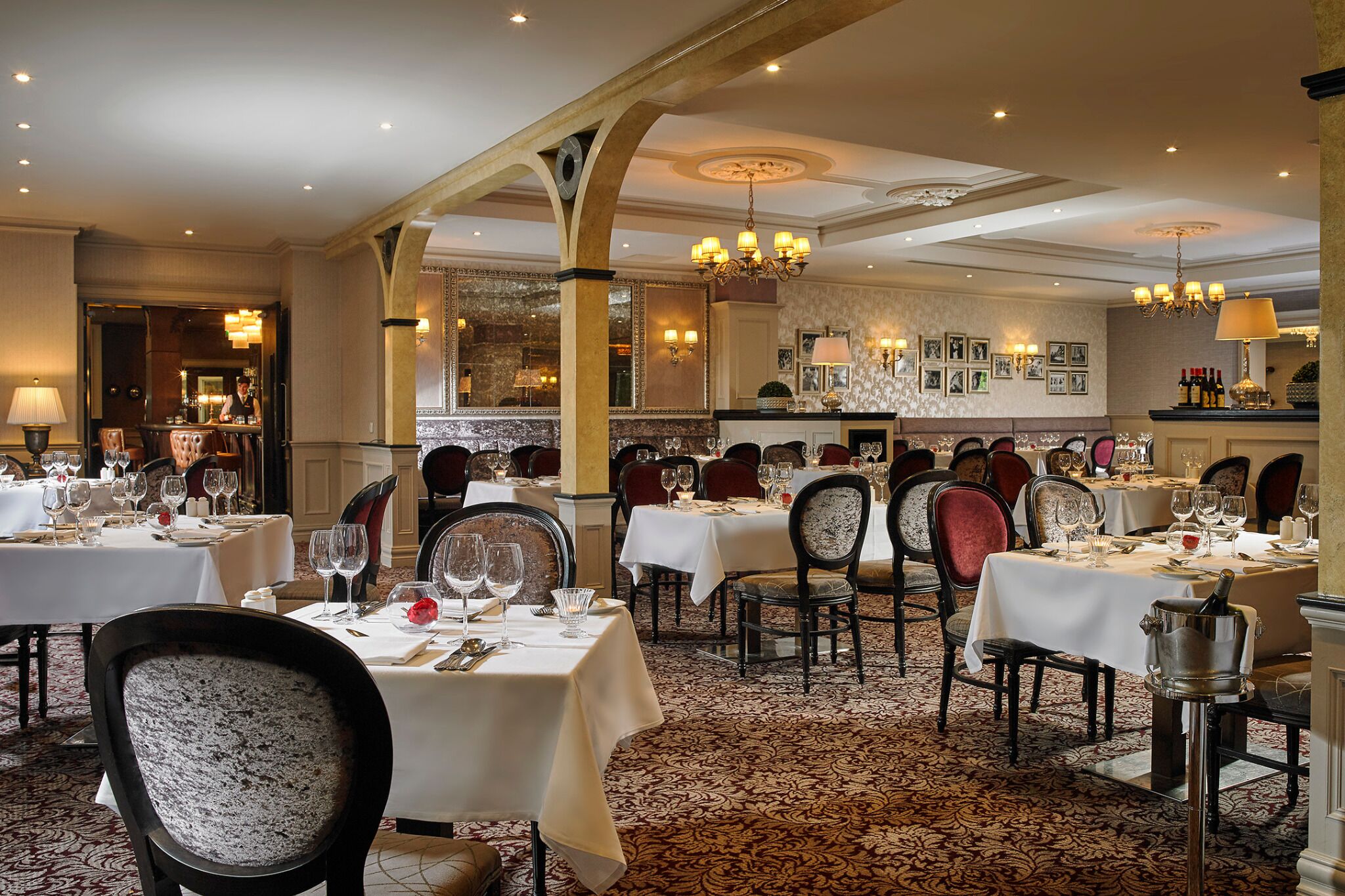 A formal dining area with multiple tables, chairs, and chandeliers.
