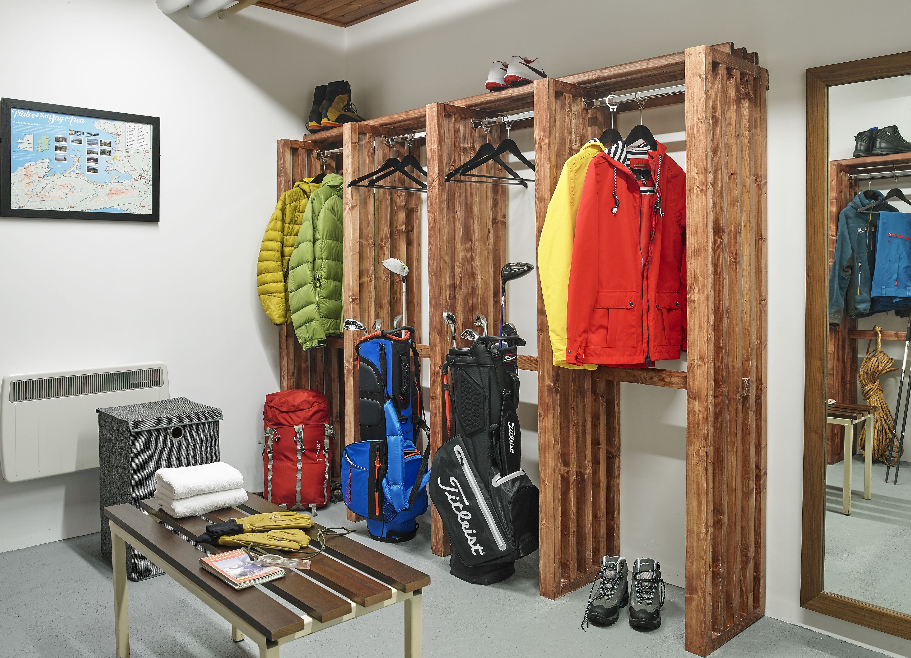 Una habitación con un perchero de madera que sostiene chaquetas, una mesa con una revista y un par de zapatos, y un mapa en la pared.