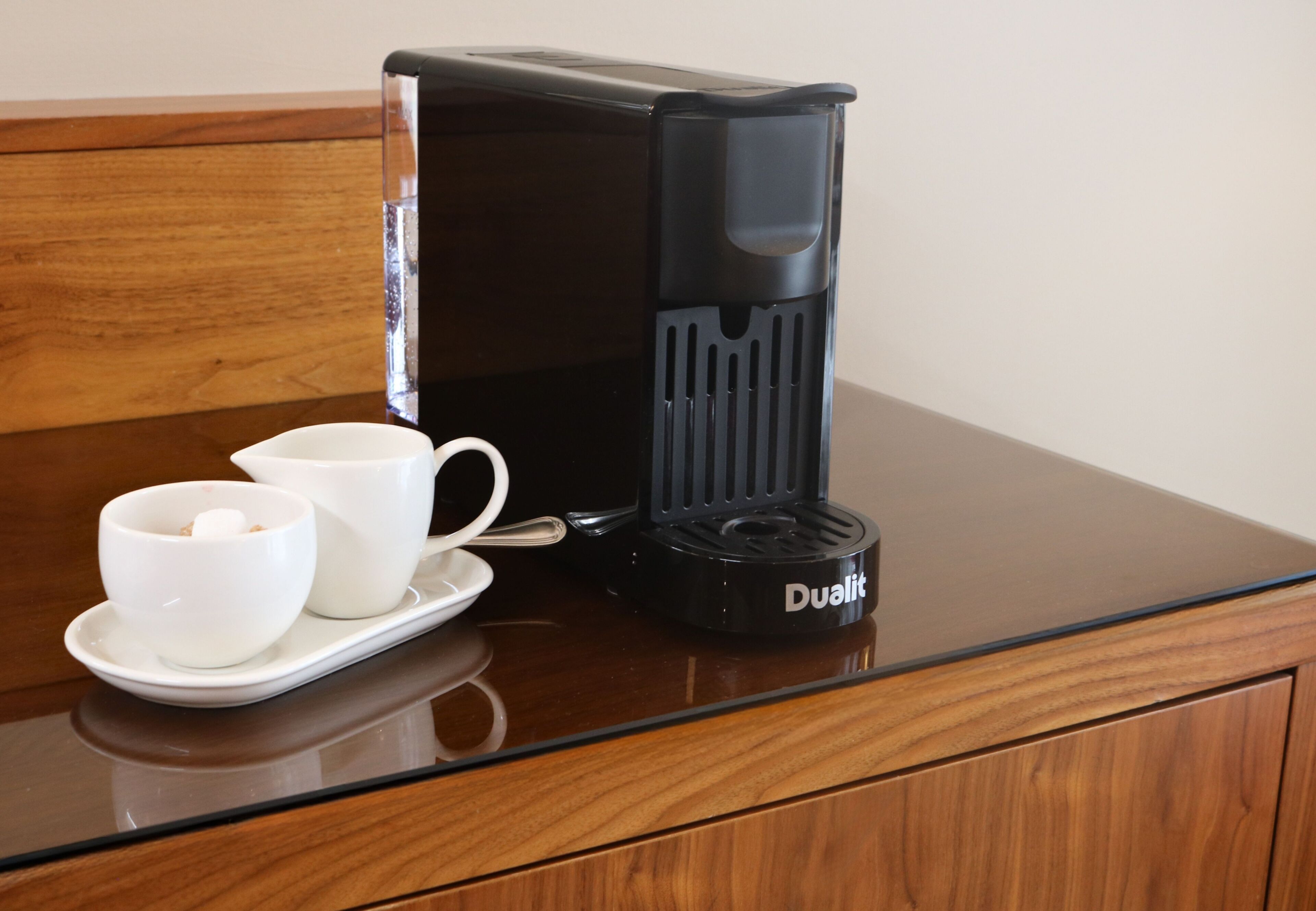Une machine à café noire est posée sur une table en bois, accompagnée de deux tasses et sous-tasses blanches.