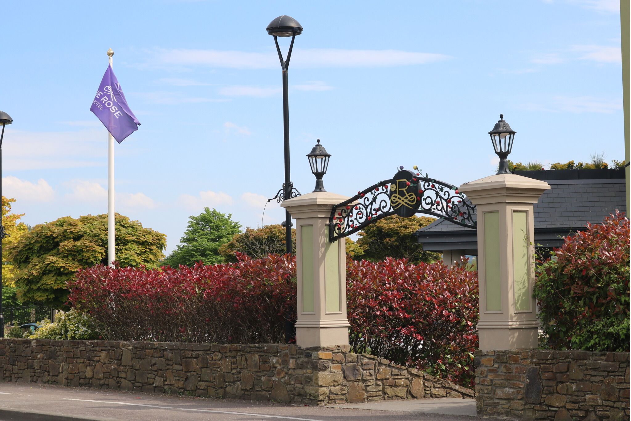 A stone wall with a wrought iron gate, a flag, and a street lamp.