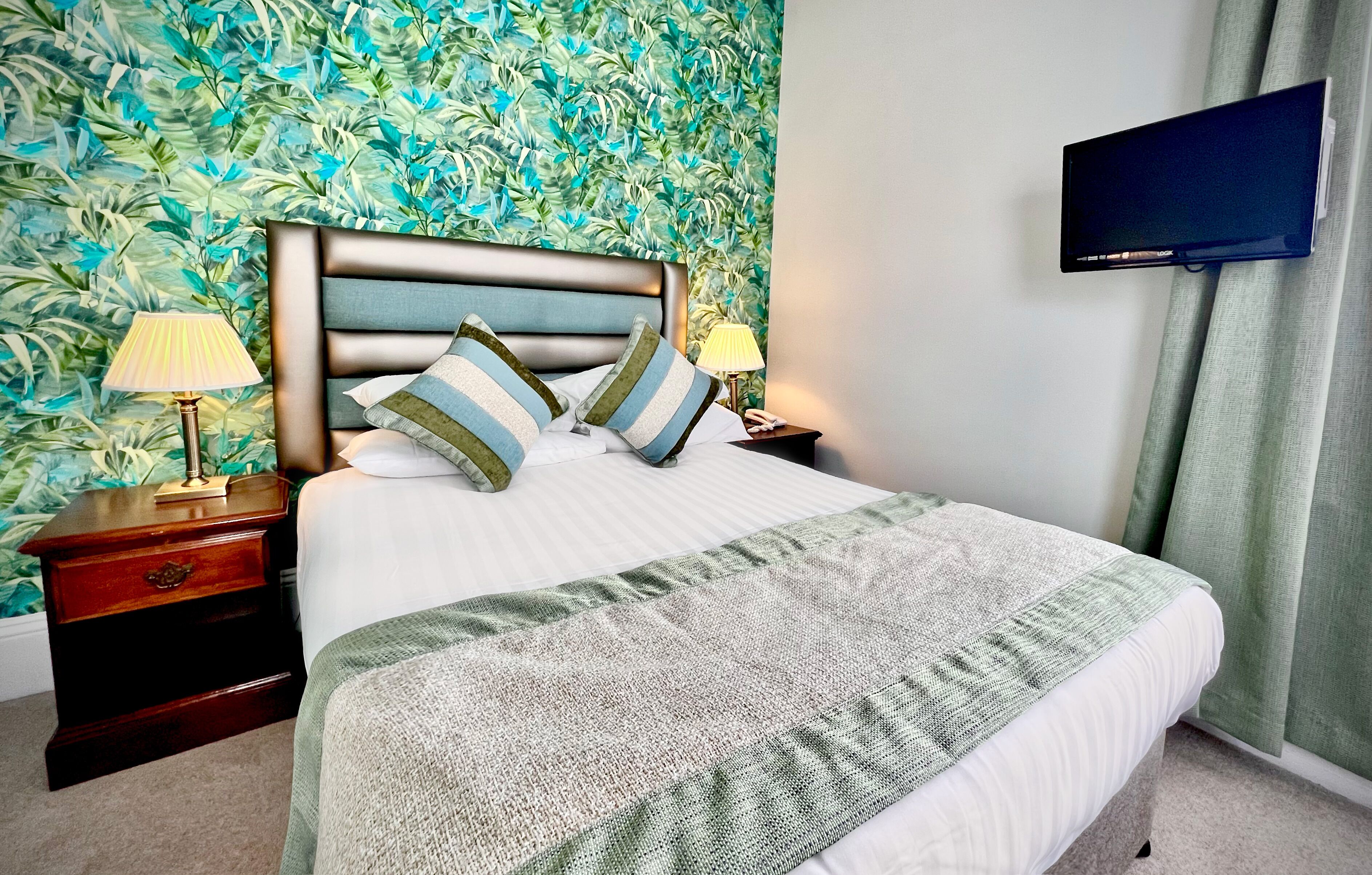 A neatly made bed with a striped pillow, a bedside lamp, and a television mounted on the wall.