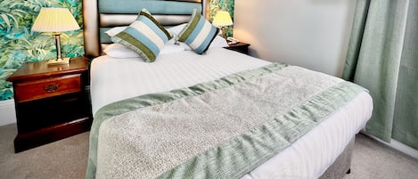 A neatly made bed with a striped pillow, a bedside lamp, and a television mounted on the wall.