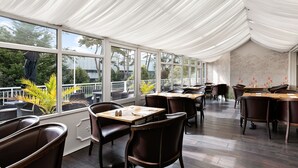 A restaurant with a covered patio, large windows, and dark wooden tables and chairs. - Abbey Sands Hotel (Torquay)