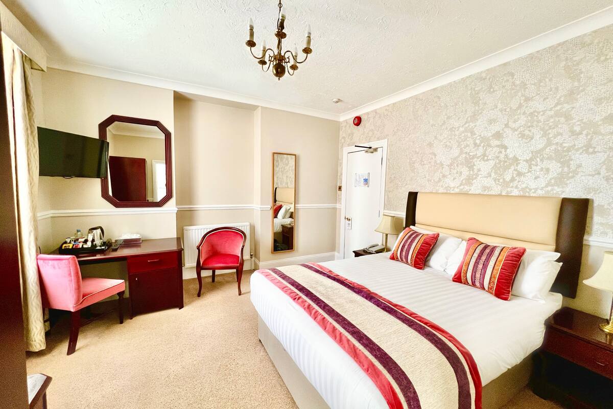 A hotel room with a large bed, a desk, a chair, and a mirror.