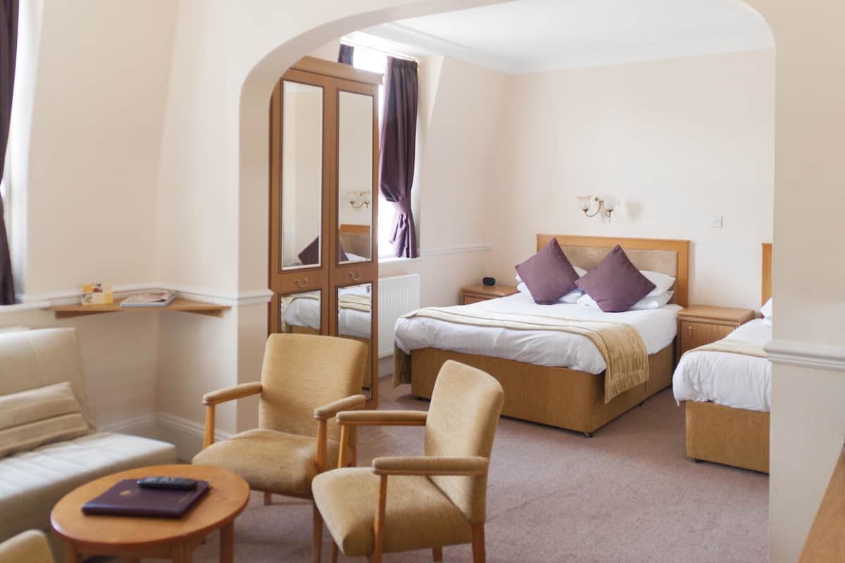 A hotel room with a bed, two armchairs, a small table, a nightstand, and a mirror.