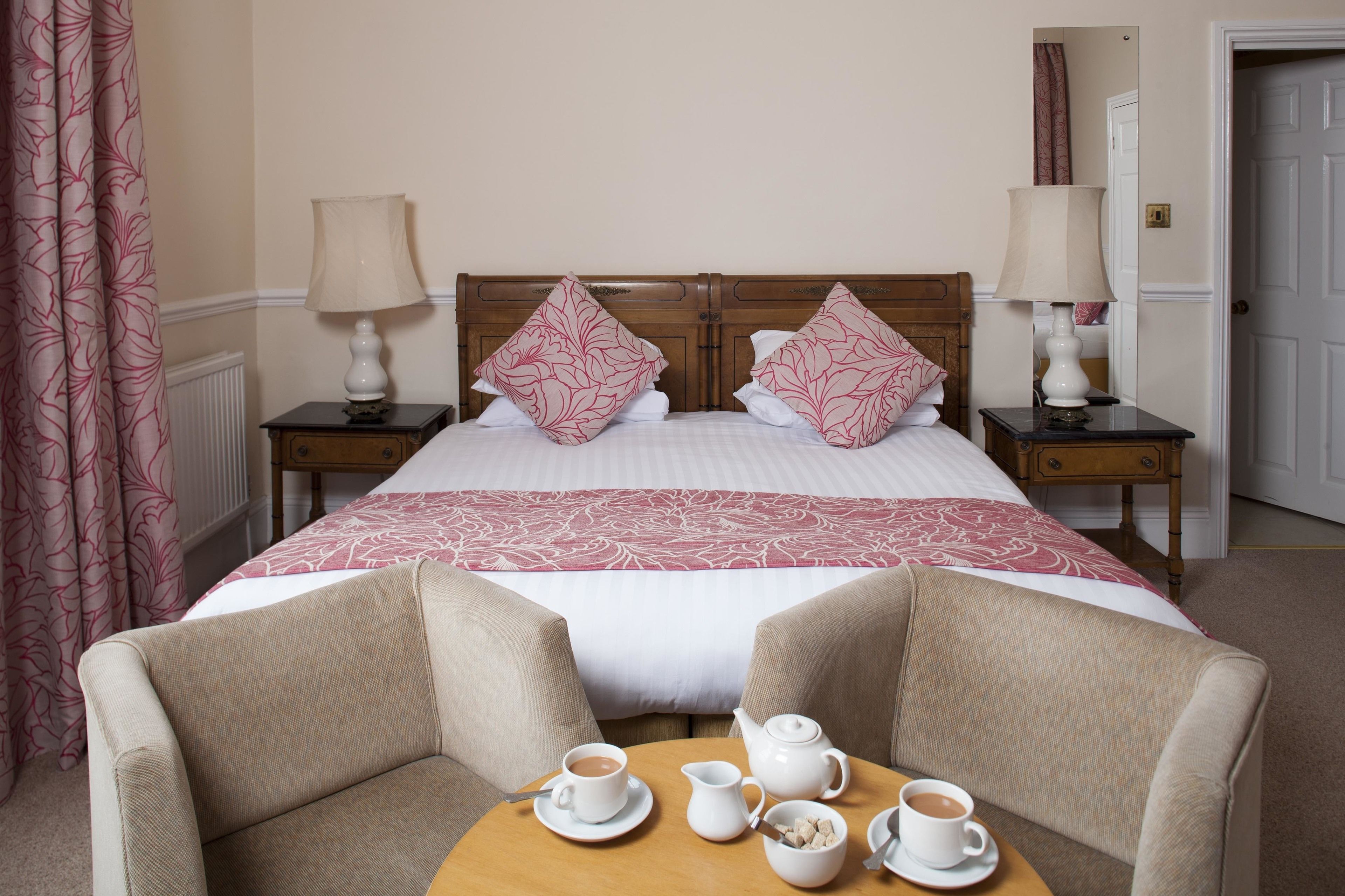 A hotel room with a large bed, two bedside tables, a wooden headboard, a table with tea set, and two armchairs.