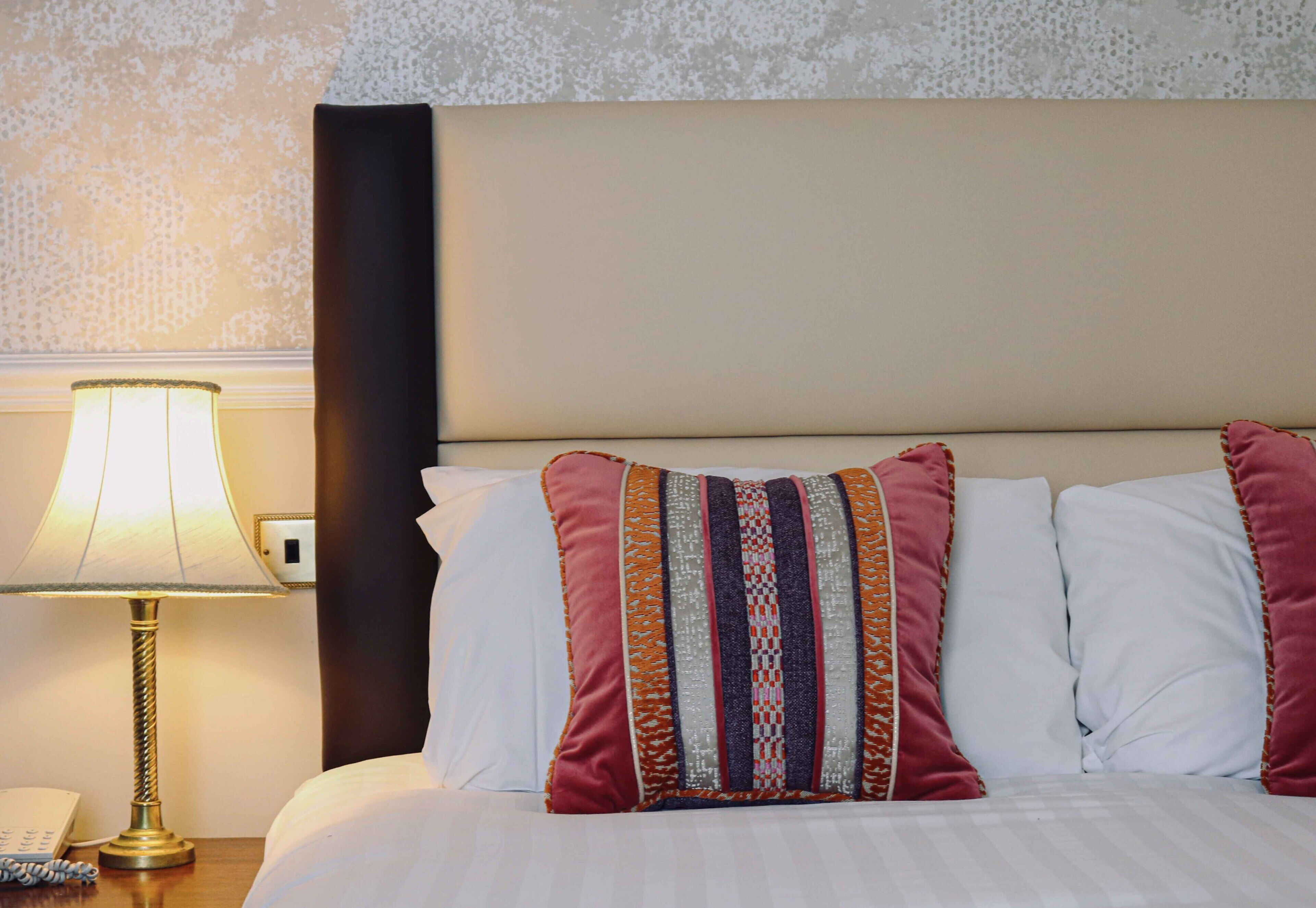 A neatly made bed with white linens and a decorative pillow with stripes.