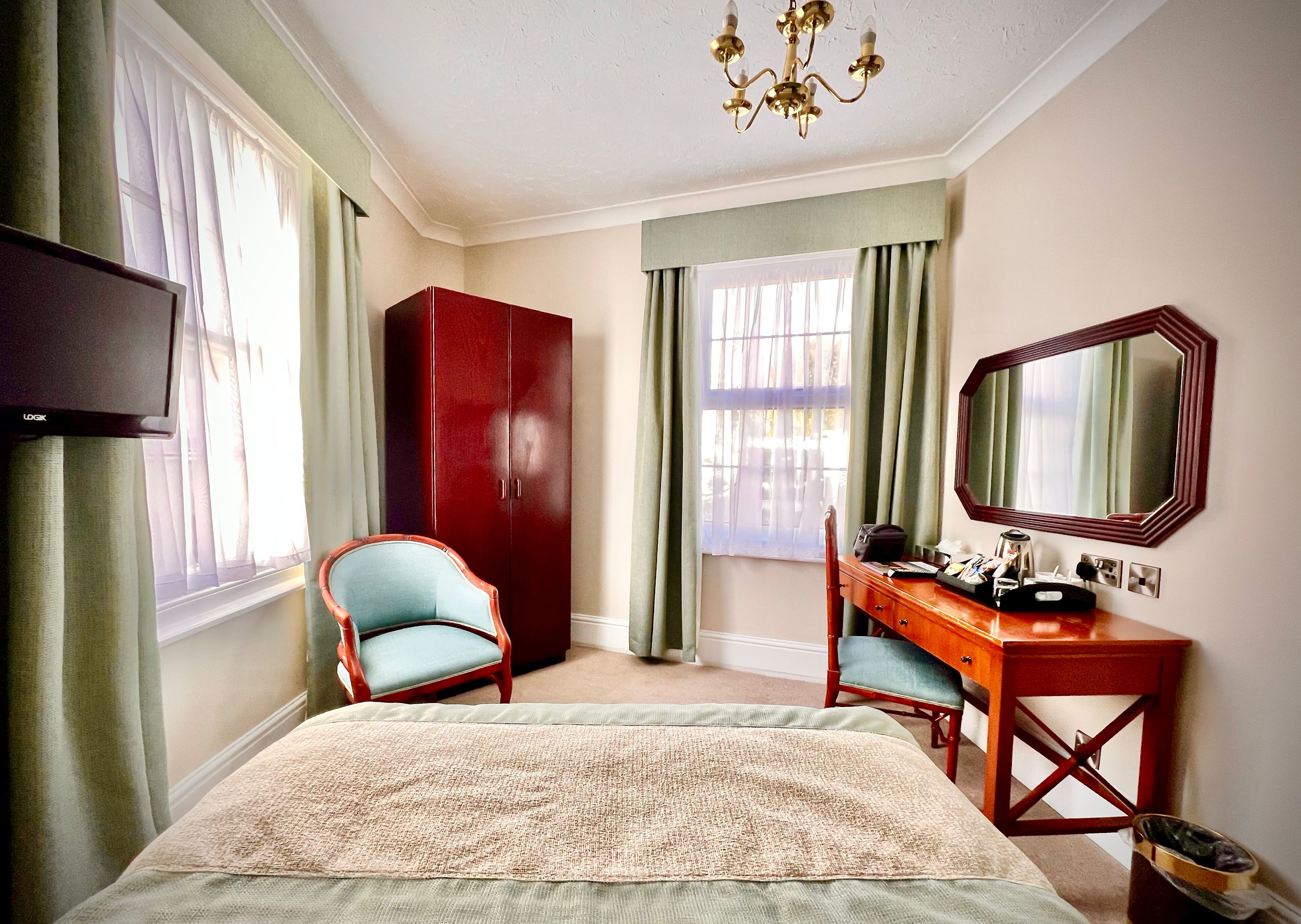 Ein Hotelzimmer mit Bett, Schreibtisch mit Stuhl, Kleiderschrank, Fernseher und großem Spiegel.
