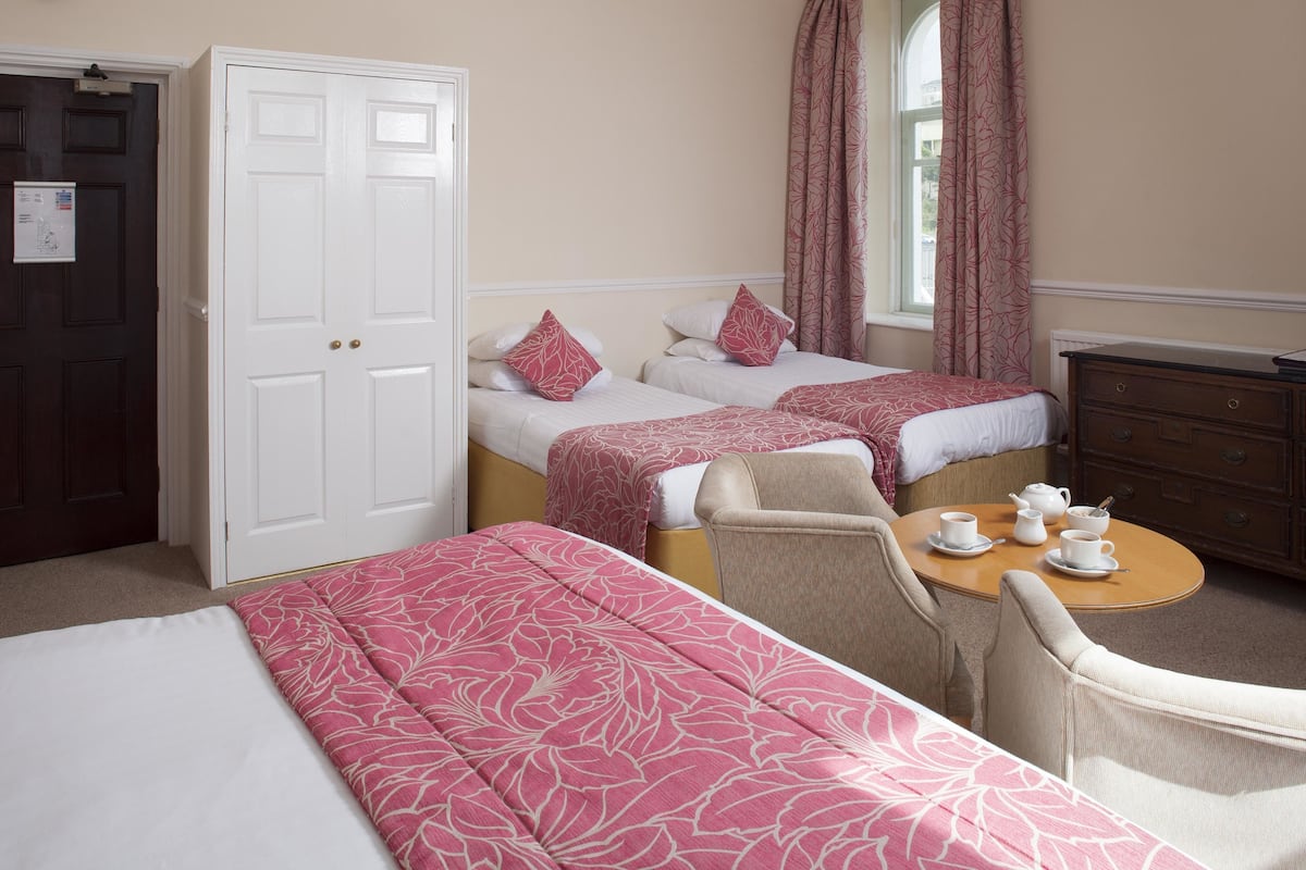 A hotel room with two beds, a sitting area with a table and chairs, and a wardrobe.