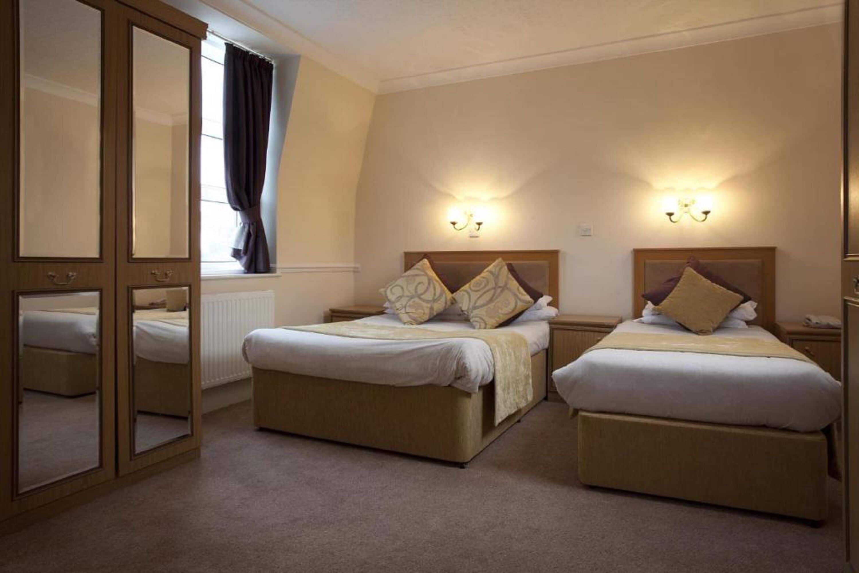 A hotel room with two beds, a large mirror, and wall-mounted lights.