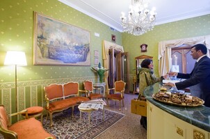 Una stanza con carta da parati verde, un quadro di grandi dimensioni, un lampadario e un banco reception con un vassoio di cibo.