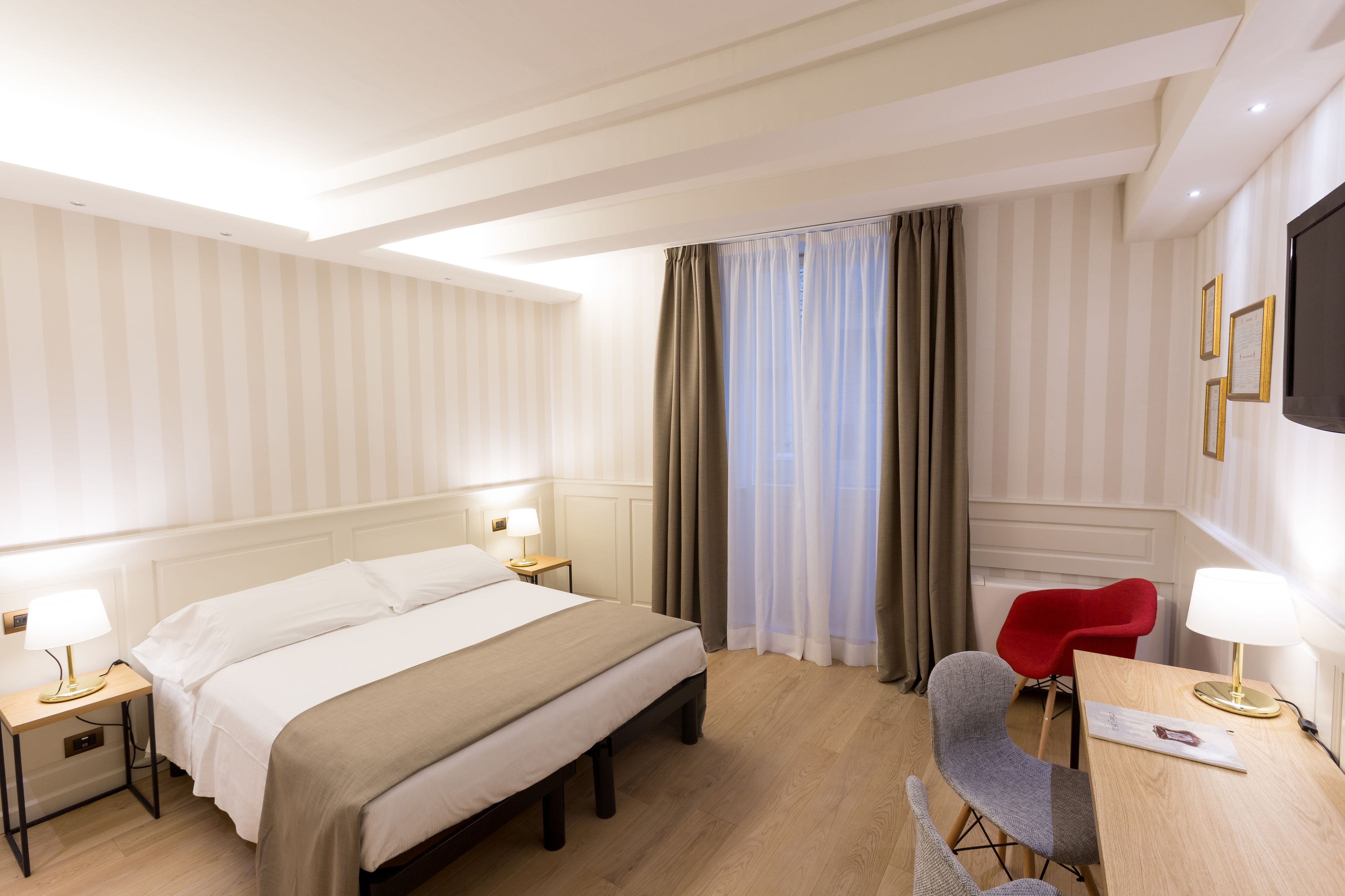 A hotel room with a bed, bedside tables, a desk, a chair, and a TV.