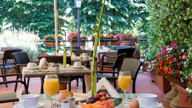 An outdoor dining area with wicker furniture, tables set with plates of fruit, eggs, and orange juice, surrounded by lush greenery and flowers. - Hotel Silla (Florence)