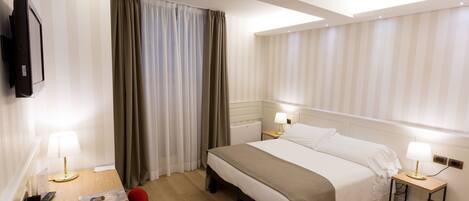 A hotel room with a bed, bedside tables, a desk with a telephone, and a television mounted on the wall.