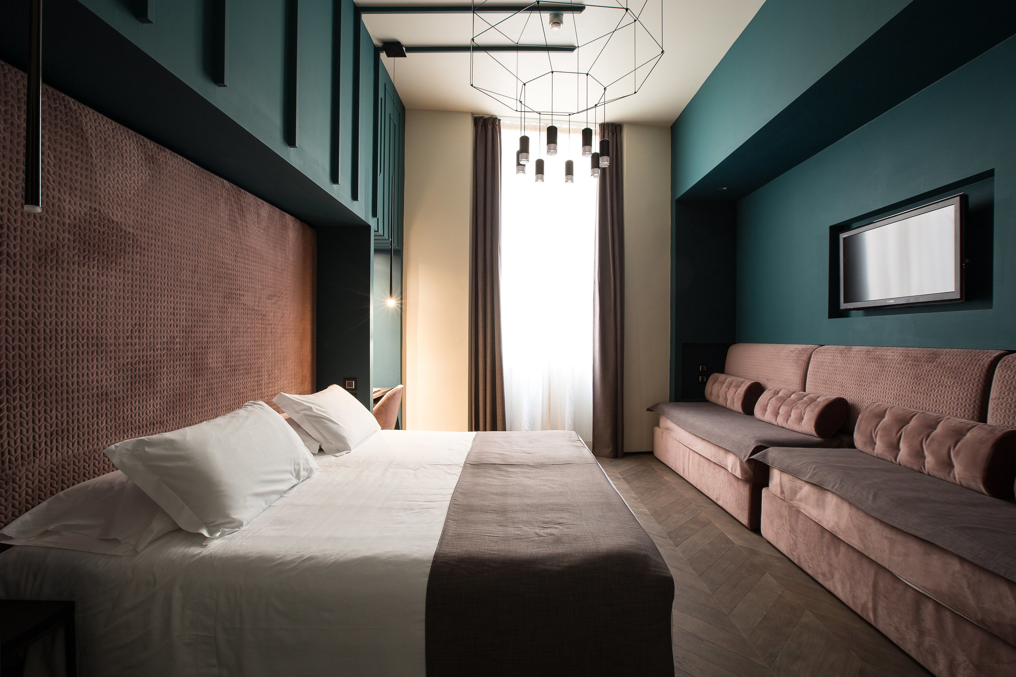 Habitación de hotel moderna con una cama grande, un sofá, un televisor y una lámpara con un diseño geométrico.