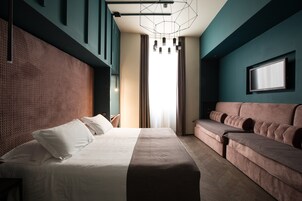 A modern hotel room with a large bed, a sofa, a TV, and a geometric light fixture.